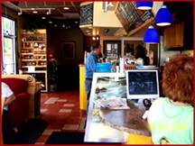 People inside a cozy Atlanta café, with one person at the counter enjoying chocolate coffee and another using a computer near the front.
